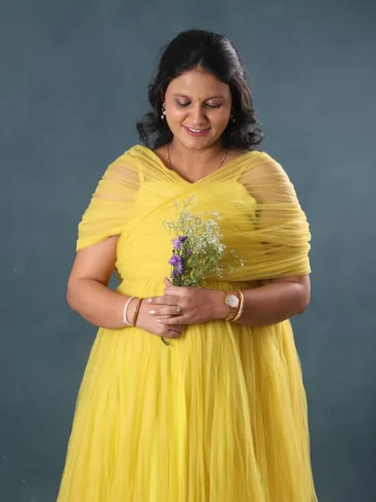 A simple and elegant studio portrait. The bright yellow off-shoulder gown and a small bouquet of flowers create a cheerful and classic maternity look.