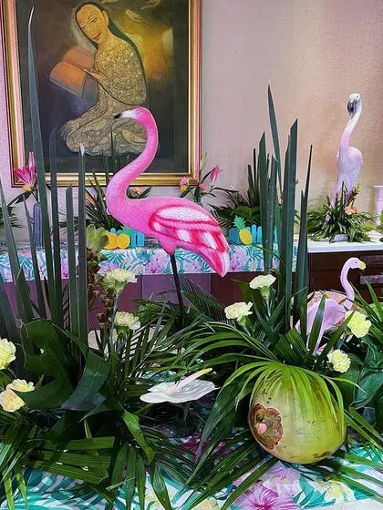 A long table decorated with a dense arrangement of tropical foliage, coconuts, and flamingo figures, creating an immersive jungle-like tablescape.