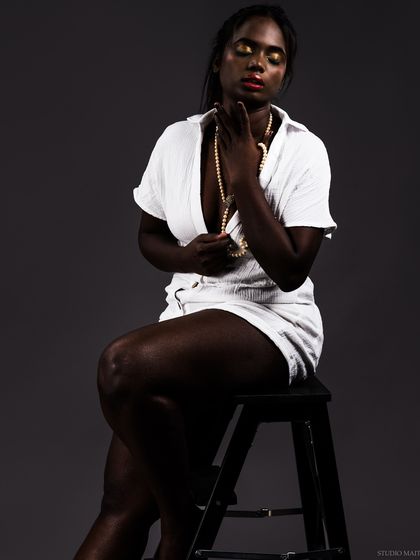 A conceptual, low-key portrait of a model with dark skin in a white outfit, creating a stunning visual contrast. This artistic series explores themes of light, shadow, and beauty.