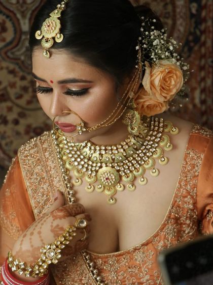 An elegant shot of a bride in a peach-colored lehenga. The oversized Kundan and pearl jewellery set she rented from us adds a touch of opulence.