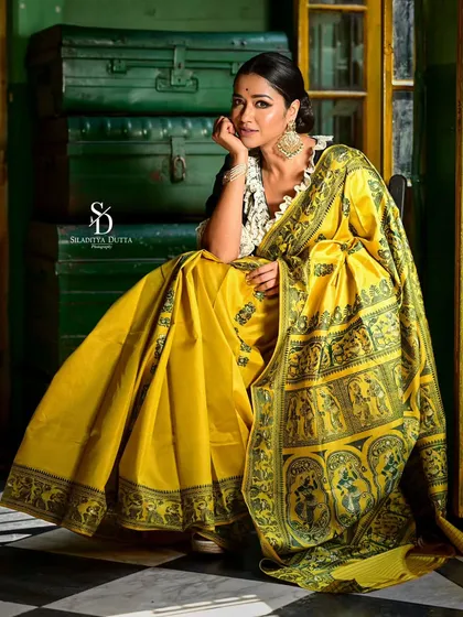 A full-length shot of Sohini seated against a stack of vintage trunks. This creative composition adds a nostalgic and artistic element to the festive fashion shoot.