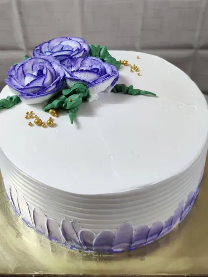 An elegant and simple white cake, perfect for any special occasion. It's decorated with beautifully piped purple frosting roses and a scattering of tiny gold beads for a sophisticated touch.