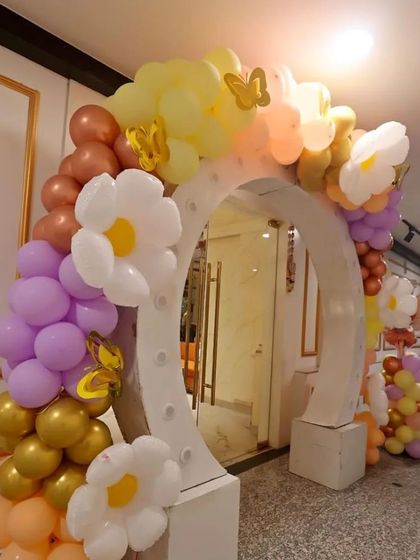 The lighted entrance arch for the flower and butterfly party, decorated with pastel balloons, daisy accents, and gold butterflies.