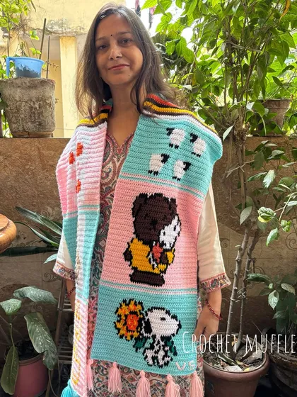 Here is my mom, Nirmala, proudly showing off a one-of-a-kind tapestry muffler we made for a customer. It features fun cartoon characters like Snoopy, sheep, and ducks, all hand-stitched with love. We can create a custom story just for you.