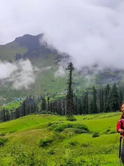 A trekker on the lush green trail of the Bhrigu Lake trek, with misty mountains in the background.