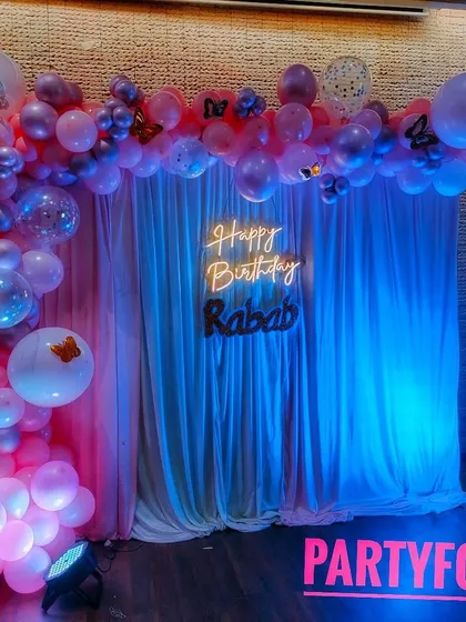 A full view of Rabab's birthday setup, highlighting the soft lighting and the elegant combination of the balloon arch and curtain backdrop.