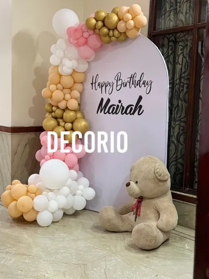 A sweet and simple teddy bear theme for a little one's birthday. The setup features a personalized arched backdrop for 'Mairah', a soft balloon garland, and a cute teddy bear sitting beside it.