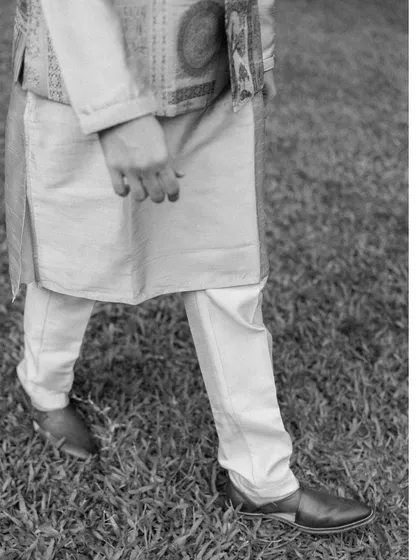 A minimalist black and white detail shot focusing on the groom's traditional kurta and shoes as he walks on the grass.