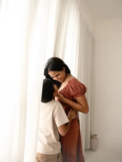 A quiet, intimate moment by the window. The soft natural light enhances the feeling of peace and love between this mother and her son.