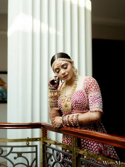 The bride leans against a balcony railing, a picture of grace and elegance. This portrait captures a quiet moment of reflection on her special day.