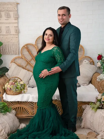 A formal and elegant couple's portrait. Dressed in coordinating emerald green outfits, the couple stands together, their hands gently placed on the baby bump. This shot is perfect for a timeless family heirloom.