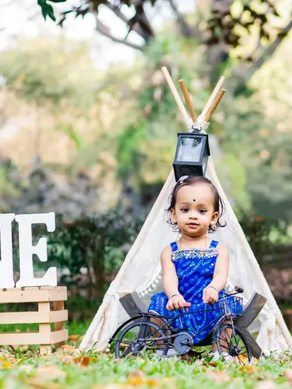 A little girl in a beautiful blue dress poses for her pre-birthday shoot with a teepee, globe, and other travel-themed props.