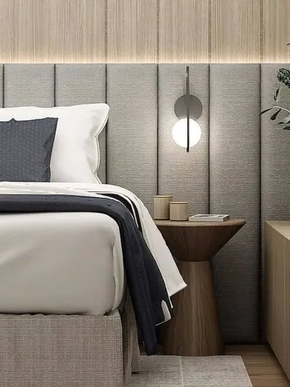 A close-up of a beautifully styled bed with a padded headboard and a modern wall lamp. The use of wood and fabric creates a warm and inviting atmosphere.