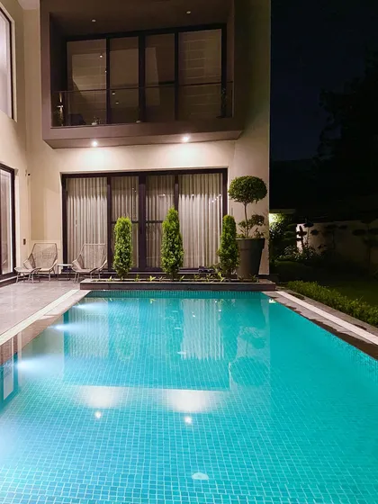 The pool at night, with underwater lights creating a magical glow. The reflection of the home's warm interior lights on the water adds to the serene ambiance.