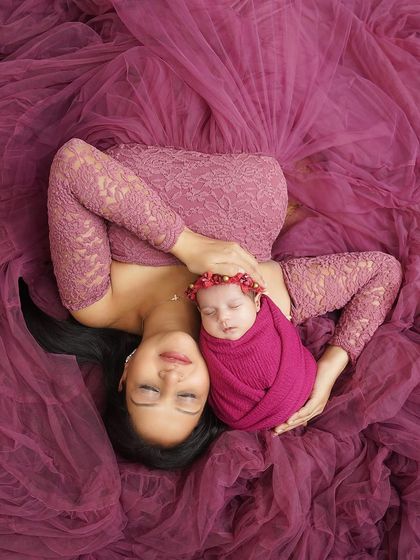 A mother's peaceful moment with her baby. Lying amidst a sea of pink tulle, she holds her sleeping daughter, creating a soft and dreamy portrait.