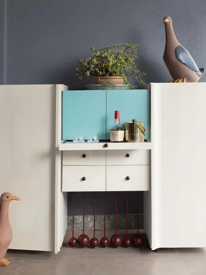 This compact bar cabinet unfolds to reveal a surprisingly spacious interior. The clean white exterior is contrasted with a pop of turquoise inside, complete with drawers and custom holders. The playful, spherical legs add a touch of whimsy to the modern design.