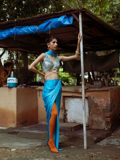 A confident, full-length pose that highlights the modern silhouette of this draped sari-style outfit. The pop of orange tights adds a bold, unexpected twist.