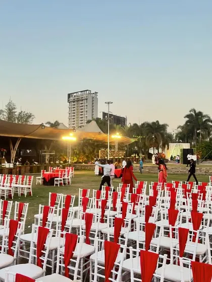 An outdoor reception setup with long rows of chairs decorated with bright red sashes, ready for the guests to arrive.
