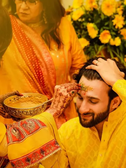 A traditional moment during the groom's Haldi ceremony. The application of the turmeric paste is a significant ritual, captured here with warmth and authenticity.