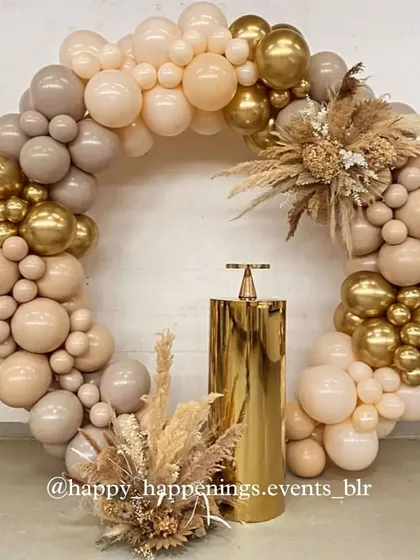 This circular balloon arrangement in nude and gold tones creates a stunning focal point for any event. The gold pedestal in the center is ideal for showcasing a cake, and the dried floral arrangements at the base complete the cohesive boho-chic theme.