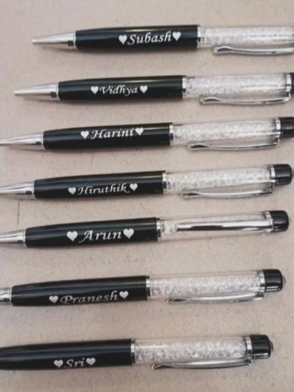 A batch of personalized crystal pens, each engraved with a name and a small heart.