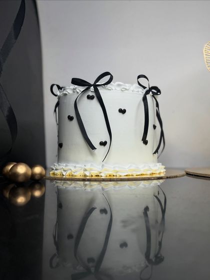 A chic and minimalist cake with black ribbons and tiny hearts. The clean white frosting and simple decorations create a modern and sophisticated look, perfect for a stylish celebration.