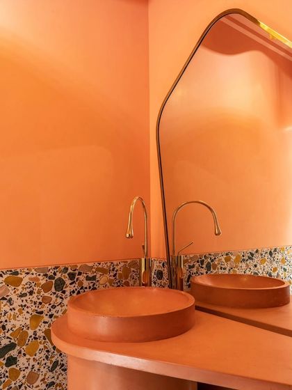 A close-up of the pink powder room highlights the custom-made concrete basin. Its color perfectly matches the pedestal and walls, creating a monolithic effect. The terrazzo and brass faucet add layers of texture and refinement.