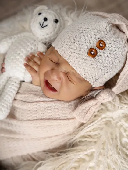 Capturing the real moments, including a little cry. This newborn, dressed in a cozy hat and swaddle, shows a fleeting expression while snuggling a teddy bear.
