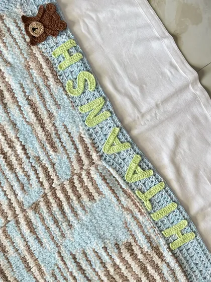 A detailed shot of the personalized name "Hitaansh" and the cute teddy bear appliqué on our knitted cuddle blanket. The letters are crocheted separately and securely stitched on.