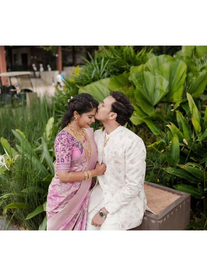 A tender forehead kiss, capturing the romance of an engagement shoot in a lush garden setting.