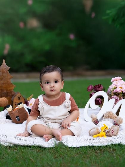 A beautiful outdoor first birthday setup. This little one is sitting peacefully on a lawn, surrounded by teddy bears and a 'One' sign, marking twelve months of love.