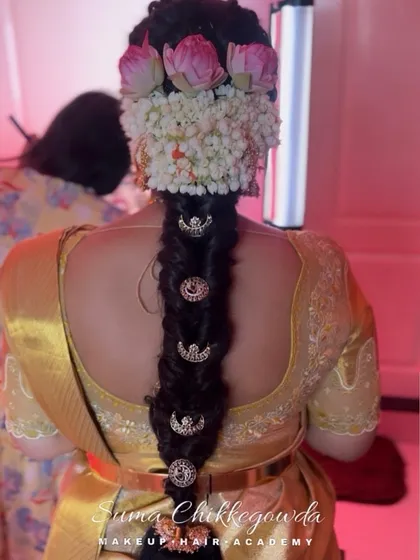 A traditional South Indian bridal look is incomplete without a beautiful hairstyle. This is a classic Jadai, a thick braid adorned with fresh jasmine and lotus flowers, creating a fragrant and absolutely stunning finish for the bride.