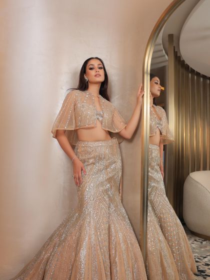 A radiant ode to elegance. This fish-cut lehenga with a graceful short cape is perfect for a modern reception look. The makeup is kept luminous and sculpted.