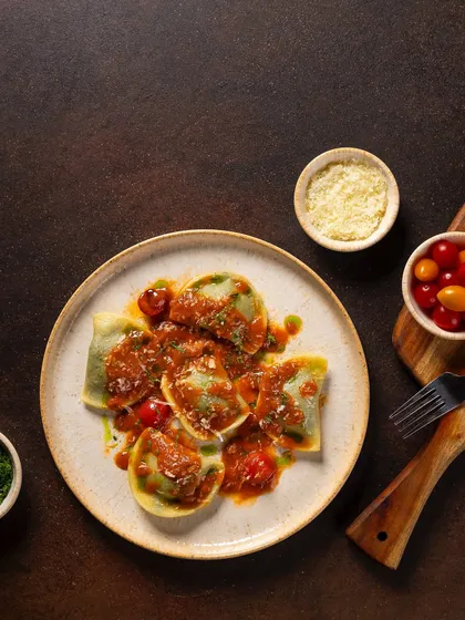 Spinach and ricotta ravioli in a tomato sauce for Novotel New Delhi. The dark, rustic background contrasts with the vibrant red of the sauce.