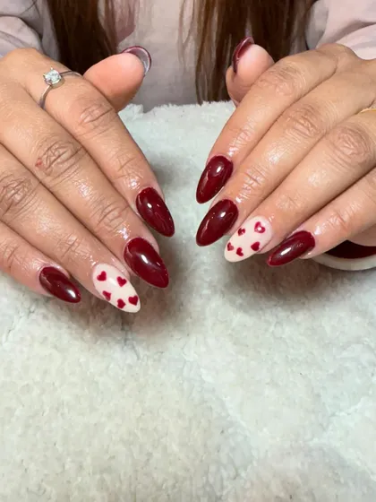 A classic Valentine's look with deep red nails and accent nails featuring tiny red hearts on a nude base. This is a simple yet very effective design.