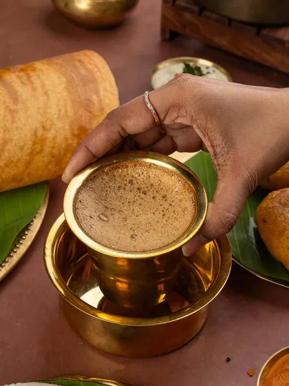 A classic South Indian filter coffee, served in its traditional brass davara. The shot captures the frothy top and rich colour, evoking authentic flavours.