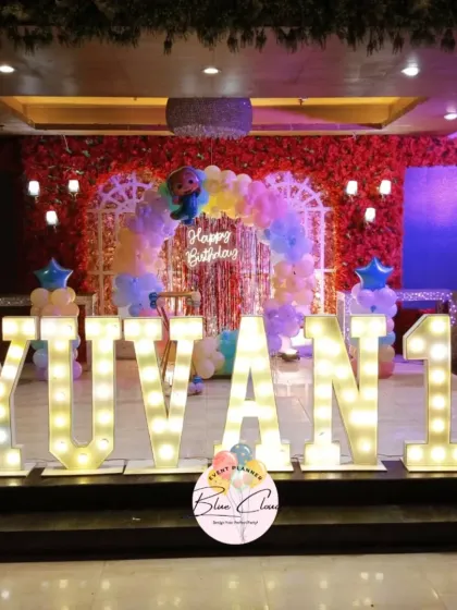 A grand stage setup for a first birthday with large marquee letters spelling 'YUVAN 1' and a pastel balloon arch.
