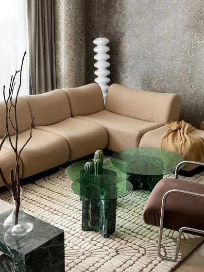 A close-up of the living room's coffee table arrangement, featuring a green glass top on a marble base. The cactus decor adds a playful, modern touch.