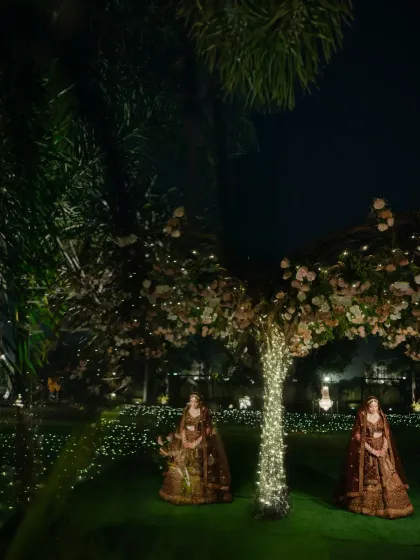 A wide, atmospheric shot of the bride in a garden at night, the fairy lights on the trees creating a magical, fairytale setting.