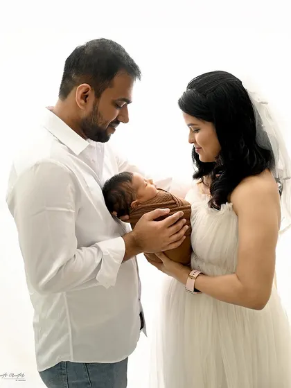 A bright and airy newborn family portrait. Dressed in all white, the parents look down at their new baby with so much love, creating a pure and angelic scene.