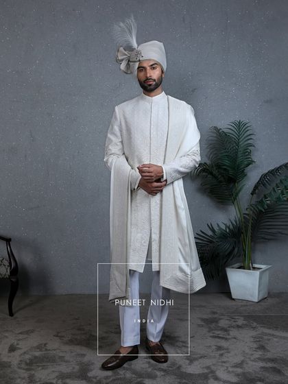 A classic ivory sherwani adorned with intricate tonal embroidery and delicate beads, paired with a pleated silk stole and ivory churidar pants, carrying the grace of tradition.