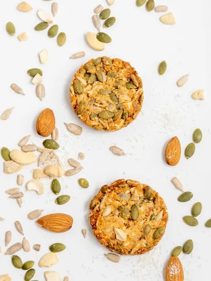 An artistic shot of our multi-seed cookies, surrounded by the raw ingredients we use. You can see the quality of the almonds, cashews, and various seeds that go into every batch.