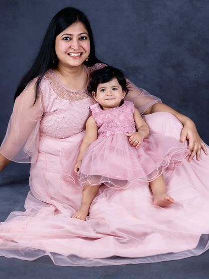 A beautiful mother-daughter portrait in matching pink dresses. The simplicity of the pose and the dark background highlight their connection.