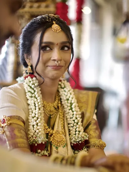 A candid shot of the bride during her Kannada wedding ceremony. Her playful, knowing glance towards the groom is an unscripted moment that reveals the deep and comfortable bond between the couple.
