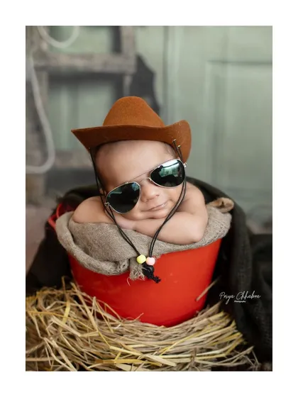 Howdy, partner! This little cowboy, complete with a hat and cool shades, is ready to wrangle some hearts. Themed shoots like this add a playful and memorable touch to your newborn's gallery.