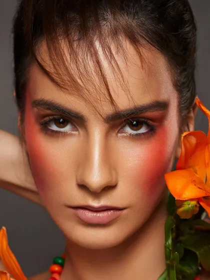 A warm, vibrant look with orange-draped blush and eyeshadow, paired with a matching orange lily.