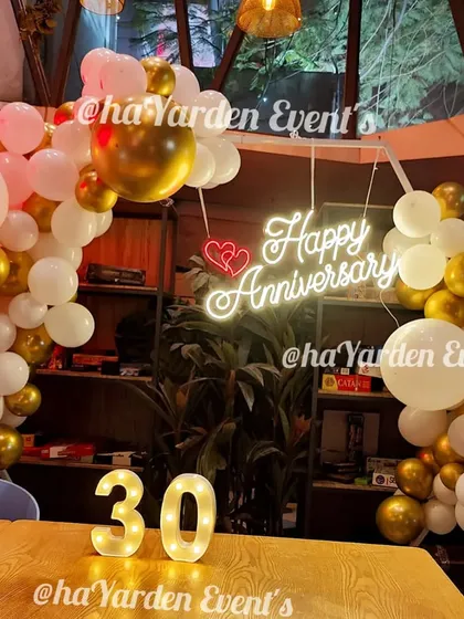 A cozy and romantic 30th anniversary celebration. The setup includes a 'Happy Anniversary' neon sign, marquee numbers, and a white and gold balloon arch.