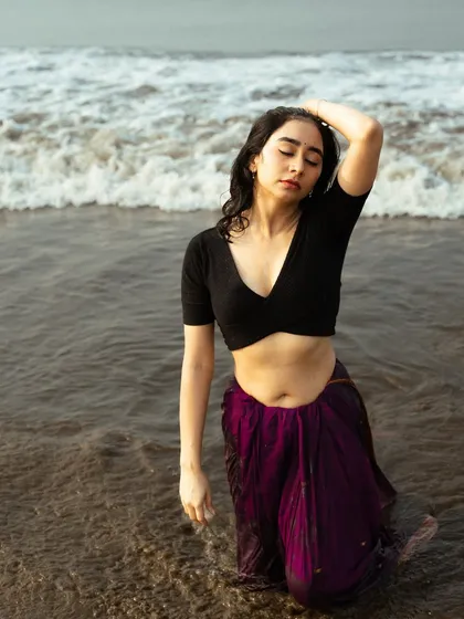 An expressive, hands-in-hair pose that feels both vulnerable and strong, with the ocean waves swirling around.
