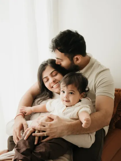 A sweet family portrait with a baby looking curiously at the camera. The father's kiss on the mother's head adds a layer of warmth and affection.