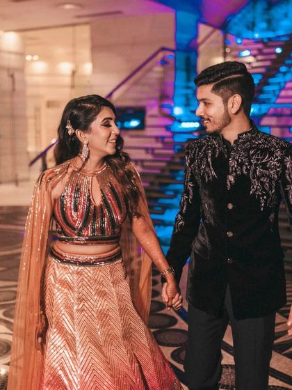 The couple holds hands as they walk through their reception venue, sharing a look of love. The neon blue lighting and modern decor create a chic, contemporary atmosphere.
